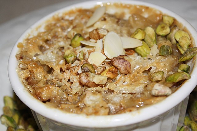 A bowl of Om Ali garnished with nuts and pistachios